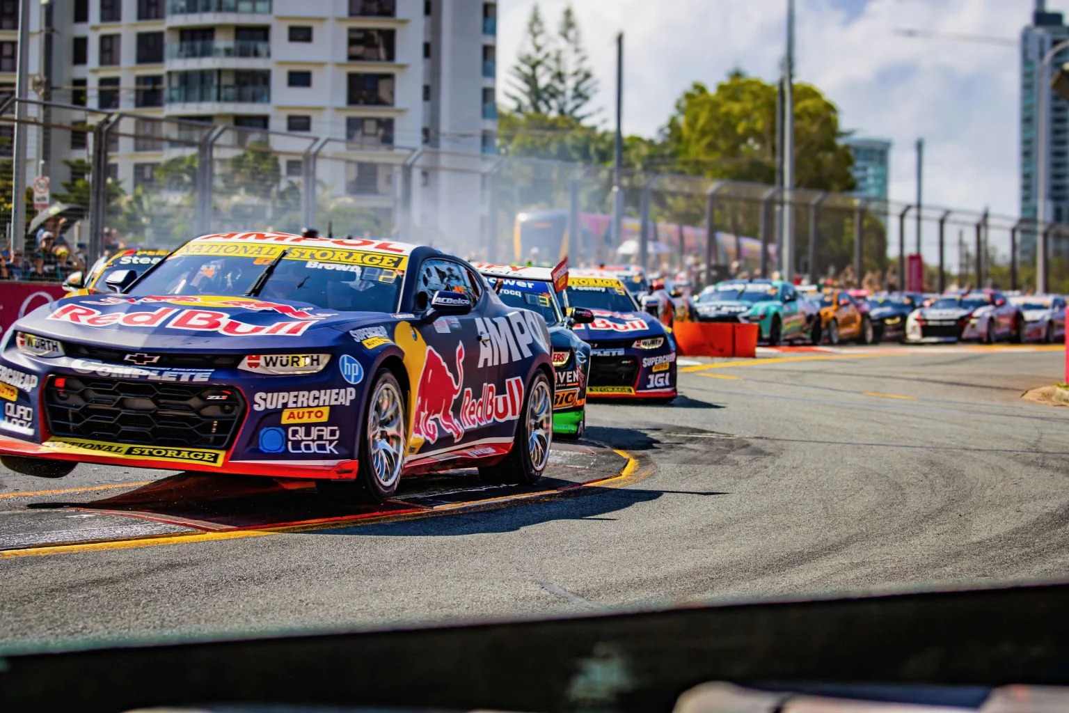 boost mobile gold coast 500 race cars rounding a street circuit corner in surfers paradise with crowds and high-rises in the background